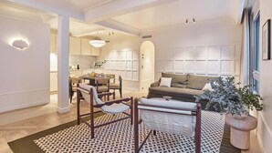 A modern living room with a sofa, chairs, a dining table, and a kitchen in the background. - Sublim AC Apartment 3 Bdr Saint Germain des Prés (Paris)