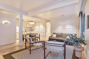 Ein modernes Wohnzimmer mit einer Couch, Sesseln, einem Esstisch und einer Küche im Hintergrund.