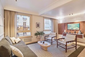 A modern living room with a sofa, armchairs, a coffee table, and a TV mounted on a wooden wall. - Sublim AC Apartment 3 Bdr Saint Germain des Prés (Paris)