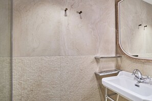 Un baño con pared de mármol, un lavabo con grifo cromado y un espejo.