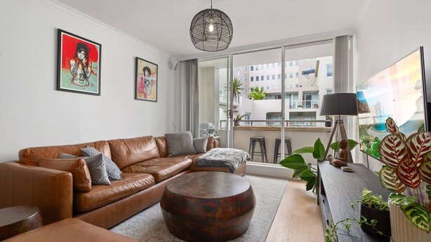 Ein modernes Wohnzimmer mit einem braunen Ledersofa, einem runden Holztisch und einem großen Fenster mit Blick auf die Stadt.