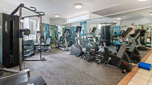 Ein Fitnessraum mit unterschiedlichen Trainingsgeräten, einer Spiegelwand und einem Teppichboden.