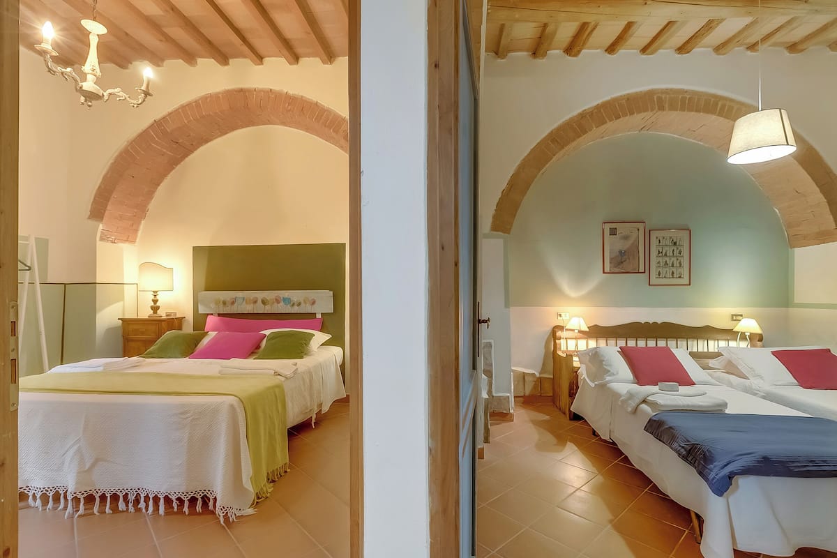 A hotel room with two beds, a brick archway, a chandelier, and a lamp.