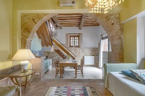 A room with a dining table, chairs, a sofa, a lamp, and a view of a kitchen through an arched doorway. - Torre Rasa Agriturismo Apartments (Castelfiorentino)