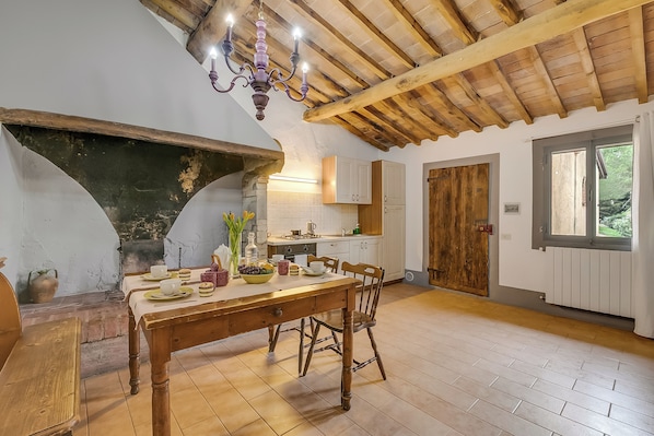 A rustic kitchen with a wooden table set for a meal, a chandelier, and a stone fireplace. - Torre Rasa Agriturismo Apartments (Castelfiorentino)