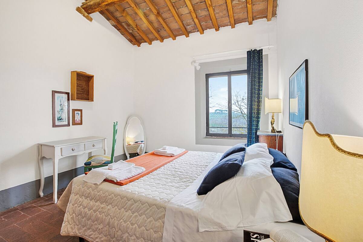 A bedroom with a bed, a desk, a window, and a mirror.
