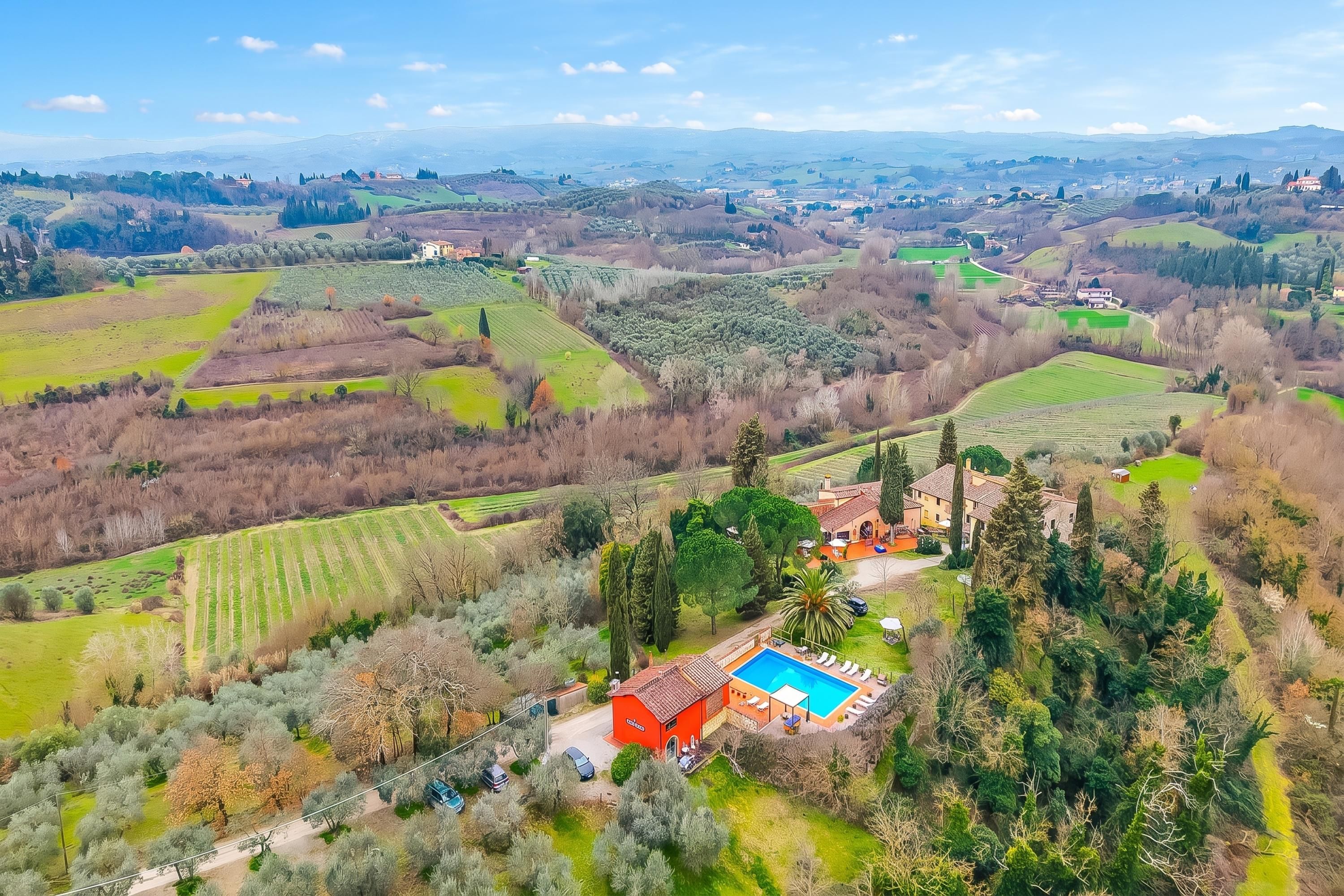 Un paysage rural avec une grande maison dotée d’une piscine, entourée de champs et d’arbres.