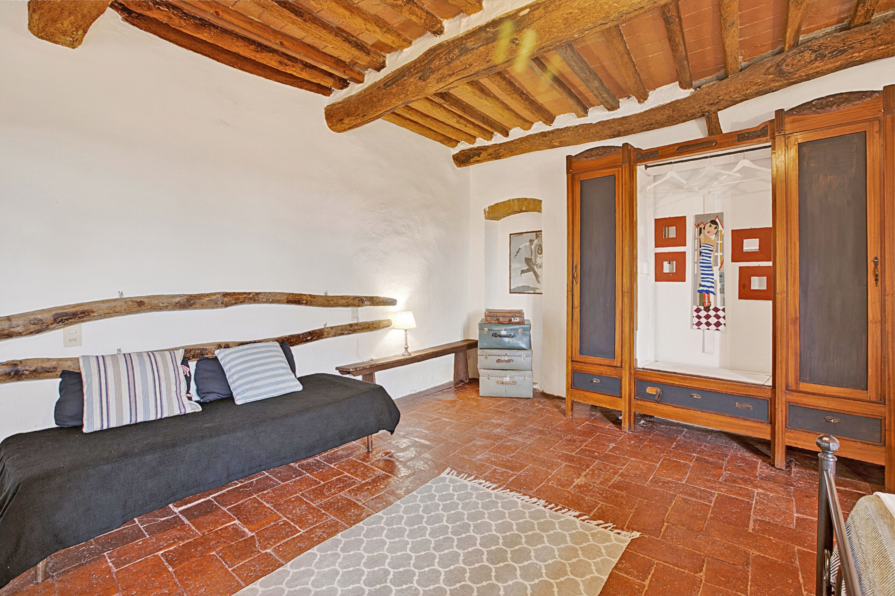 Una habitación con cama, vigas de madera, suelo de baldosas y un armario.