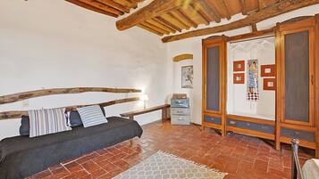 Una habitación con cama, vigas de madera, suelo de baldosas y un armario.