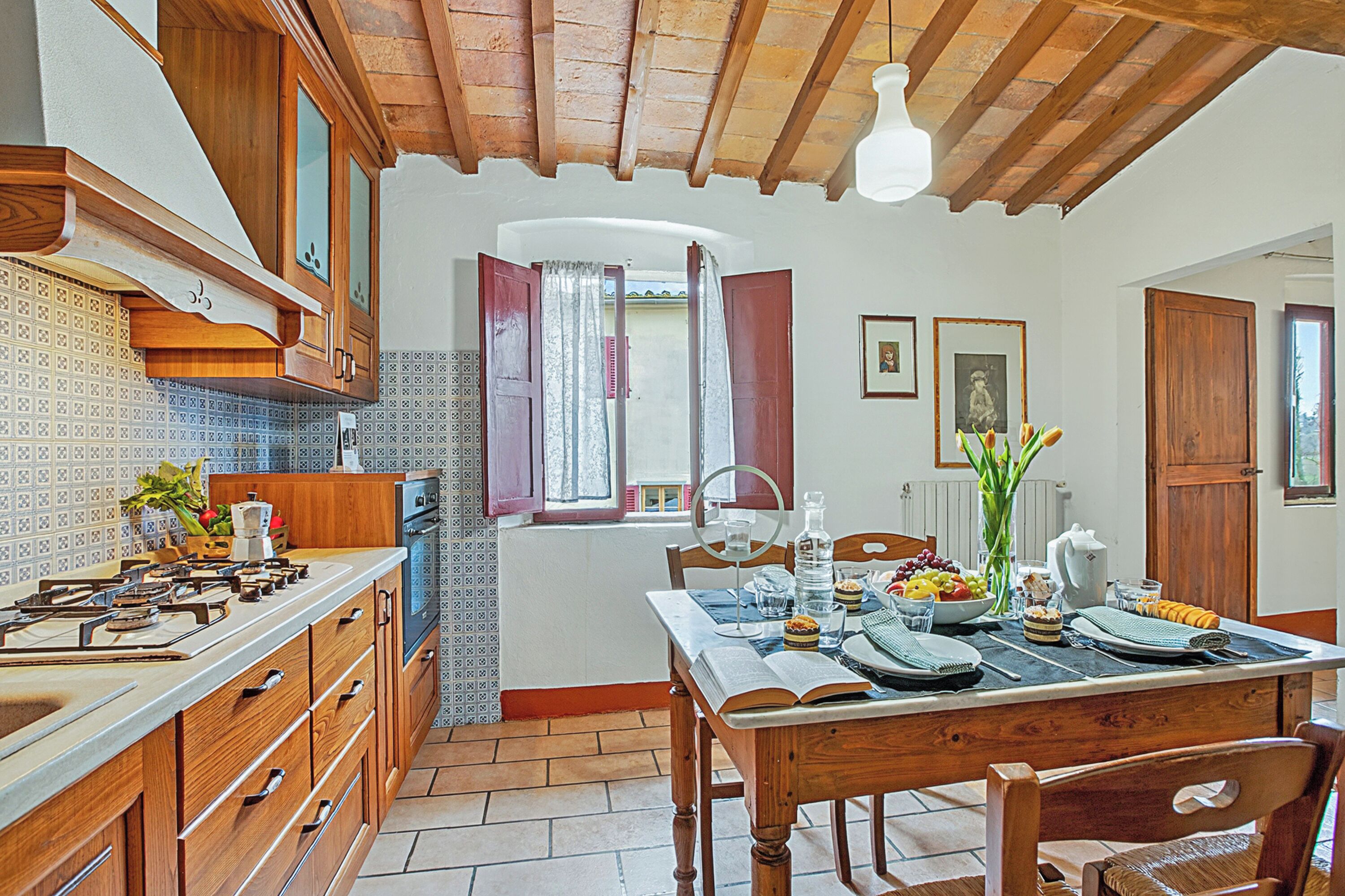 Una cocina con armarios de madera, una mesa de comedor preparada para cuatro personas y vistas al exterior a través de una ventana.