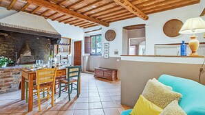 A rustic interior with a dining area, wooden ceiling beams, a fireplace, and a cozy seating area.