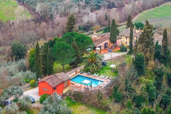 A villa with a swimming pool, surrounded by trees and a hilly landscape.
