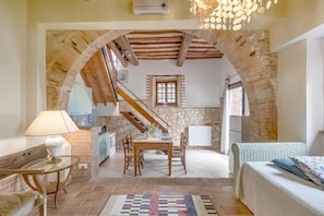 Un interior acogedor con comedor, cocina y sala de estar, que presenta vigas de madera a la vista, paredes de piedra y suelo de baldosas.