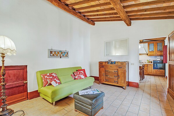 Ein Wohnzimmer mit einem grünen Sofa, einem Holzschrank und einer Küche im Hintergrund.