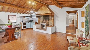 A rustic kitchen with a brick oven, wooden beams, and a dining area with a table and chairs.