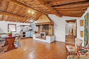 A rustic kitchen with a brick oven, wooden beams, and a dining area with a table and chairs. - Torre Rasa Agriturismo Apartments (Castelfiorentino)
