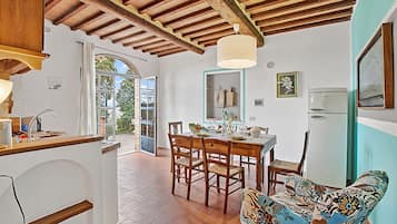Una cocina con vigas de madera, una mesa de comedor con sillas, un refrigerador y un sofá estampado.