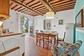 A kitchen with wooden beams, a dining table with chairs, a refrigerator, and a patterned sofa.