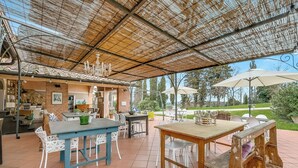 An outdoor patio with tables and chairs, a covered area with a ceiling, and a view of the surrounding landscape. - Torre Rasa Agriturismo Apartments (Castelfiorentino)