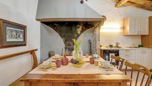 A dining area with a wooden table set for a meal, a chandelier, and a kitchen in the background.