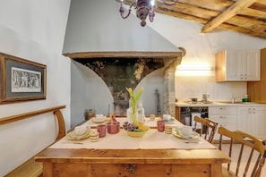 A dining area with a wooden table set for a meal, a chandelier, and a kitchen in the background. - Torre Rasa Agriturismo Apartments (Castelfiorentino)