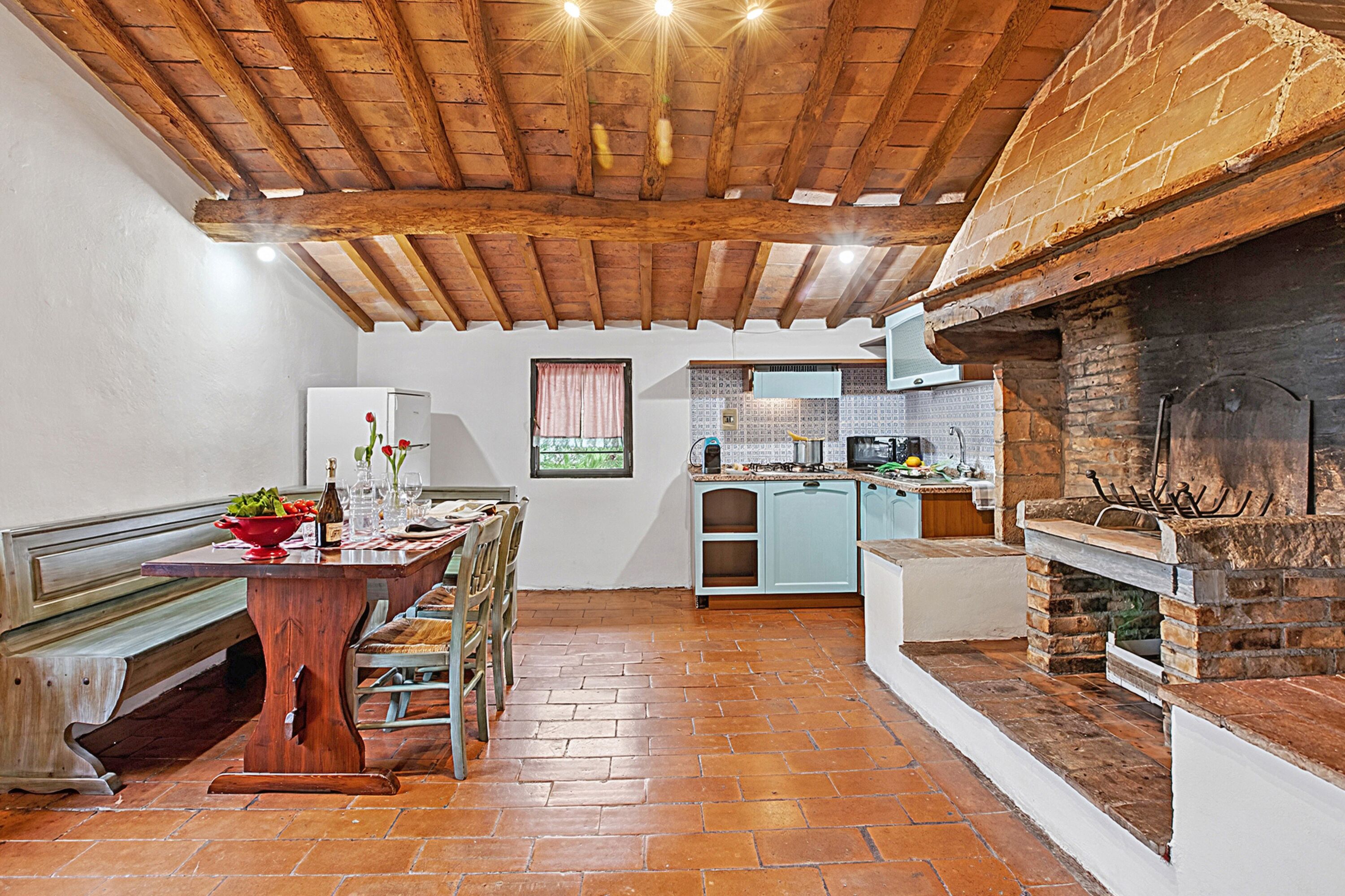 Una cocina rústica con techo de madera, chimenea de ladrillo y una zona de comedor con banco y mesa.