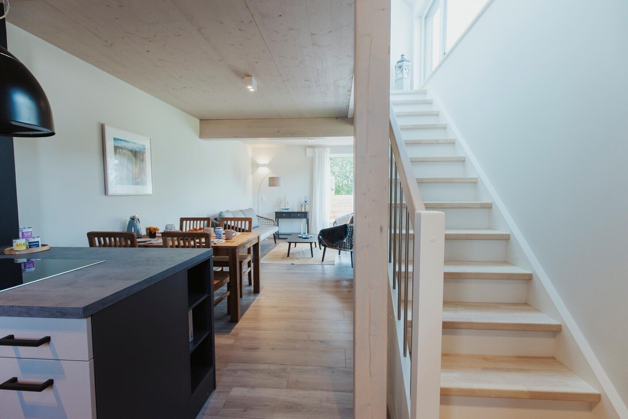A modern kitchen with a dining area, wooden staircase, and a view of the outdoors.