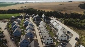 A residential area with modern houses, a parking lot, and a view of a large open field and water body in the distance.