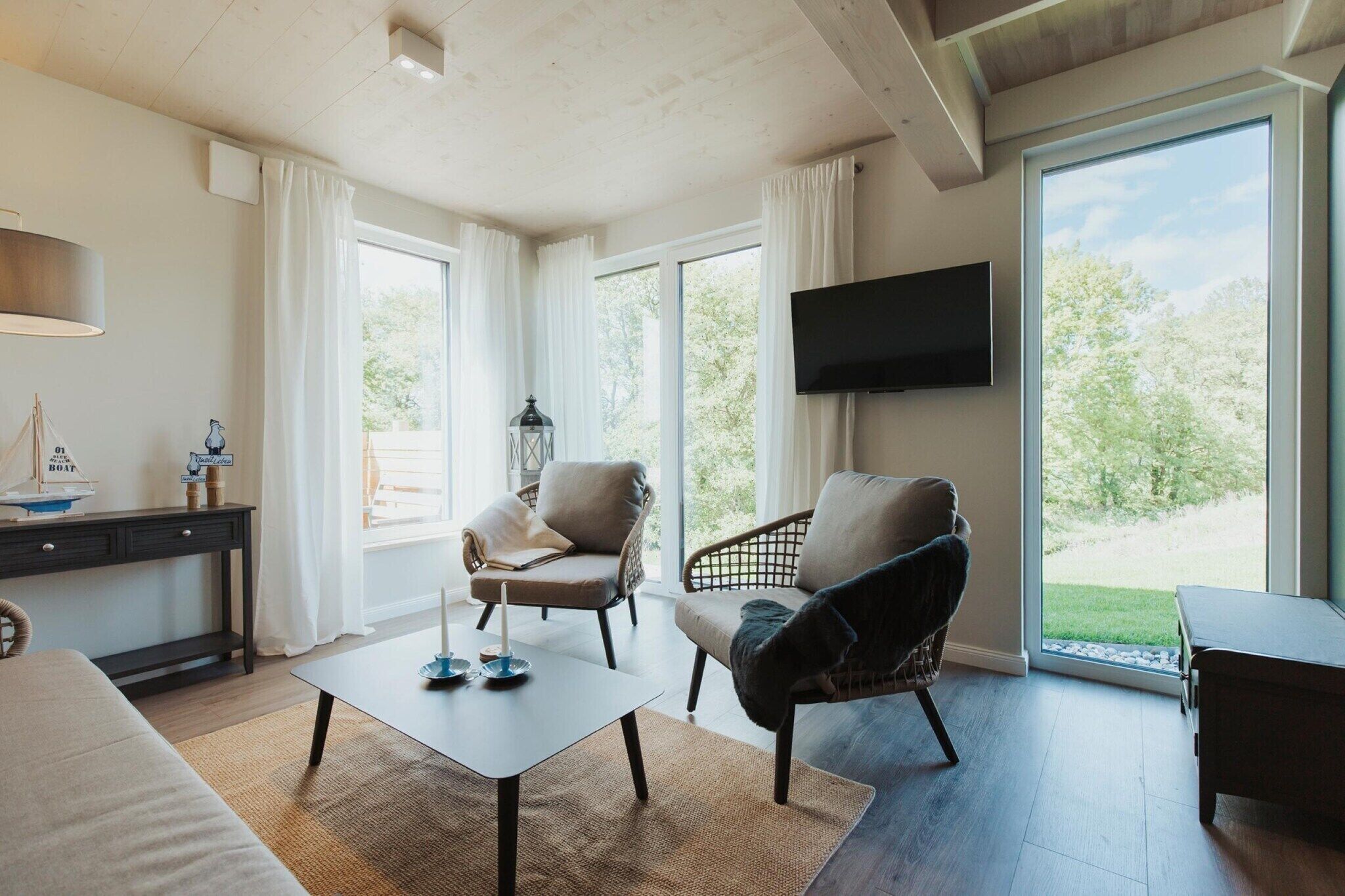 Una sala de estar moderna con un sofá, sillones, una mesa de centro, un televisor y ventanas amplias con vistas a zonas verdes.
