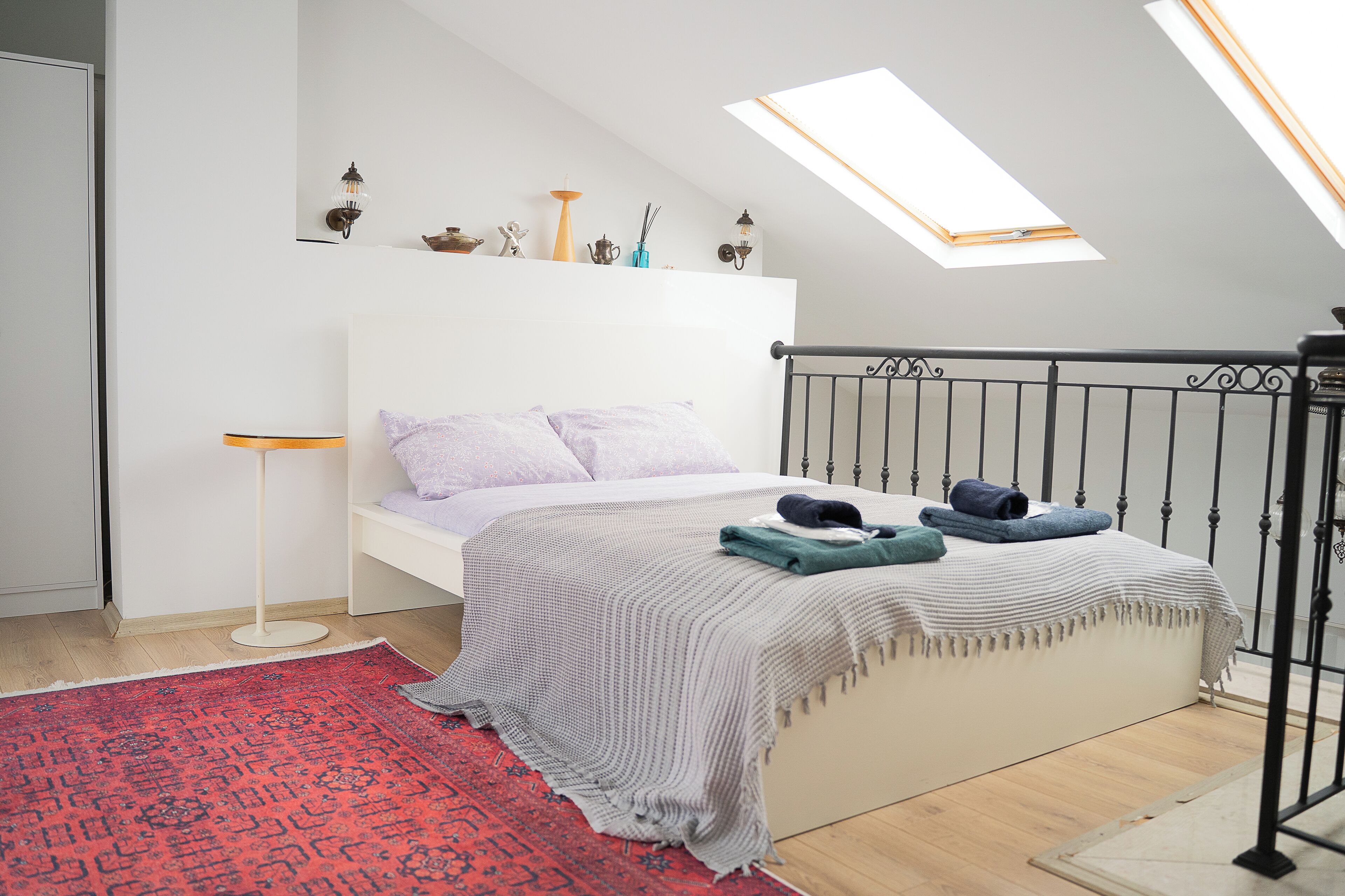 Un dormitorio con tragaluces, una cama con almohadas, una mesita de noche y una alfombra roja estampada.