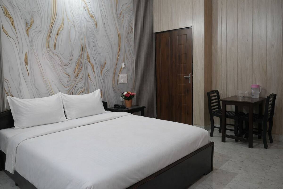 Un dormitorio con cama, mesita de noche, silla y una pequeña mesa con un florero.