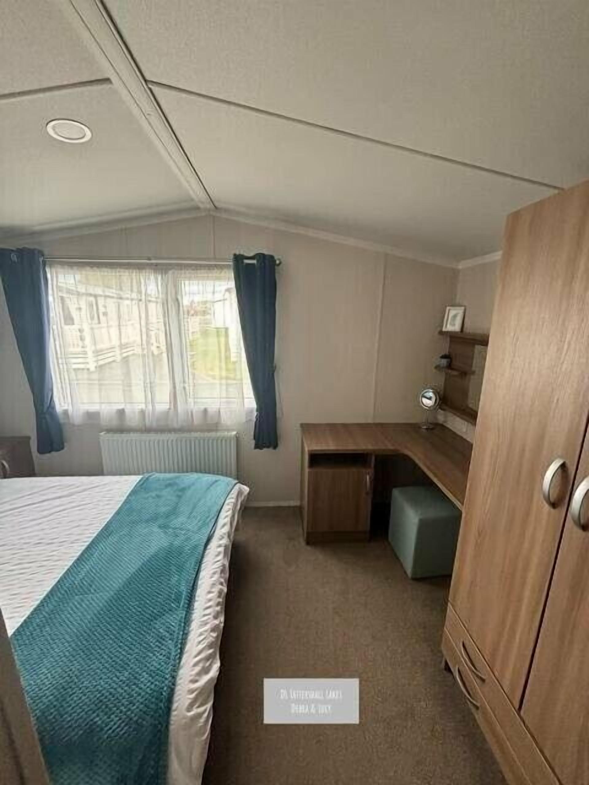 A compact room with a bed, a desk, a wardrobe, and a window with curtains.