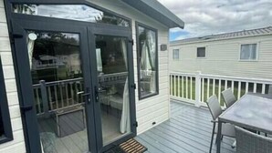 A covered deck with a glass door, a small outdoor table, and a chair. - Tattershall Lakes Country Park - Holiday Accommodation 15201 (Lincoln)
