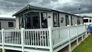 A mobile home with a fenced porch, a small attached garage, and a single-story structure. - Tattershall Lakes Country Park - Holiday Accommodation 15201 (Lincoln)