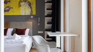 Ein Hotelzimmer mit Bett, Sessel, Schreibtisch, Bücherregal und einem Bild an der Wand.