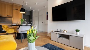 Ein modernes Wohnzimmer mit einer Couch, einem Essbereich mit Stühlen, einem an der Wand montierten Fernseher und einem weißen Schrank.