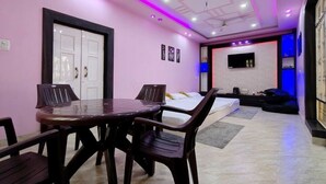 A room with a dining table, chairs, a bed, a TV, and a ceiling fan. - Cozy Nirmala House Homestay in Varanasi (Varanasi)