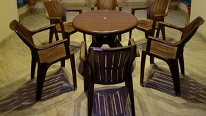 A covered outdoor seating area with a round table and chairs, potted plants, and a view of buildings in the background. - Cozy Nirmala House Homestay in Varanasi (Varanasi)
