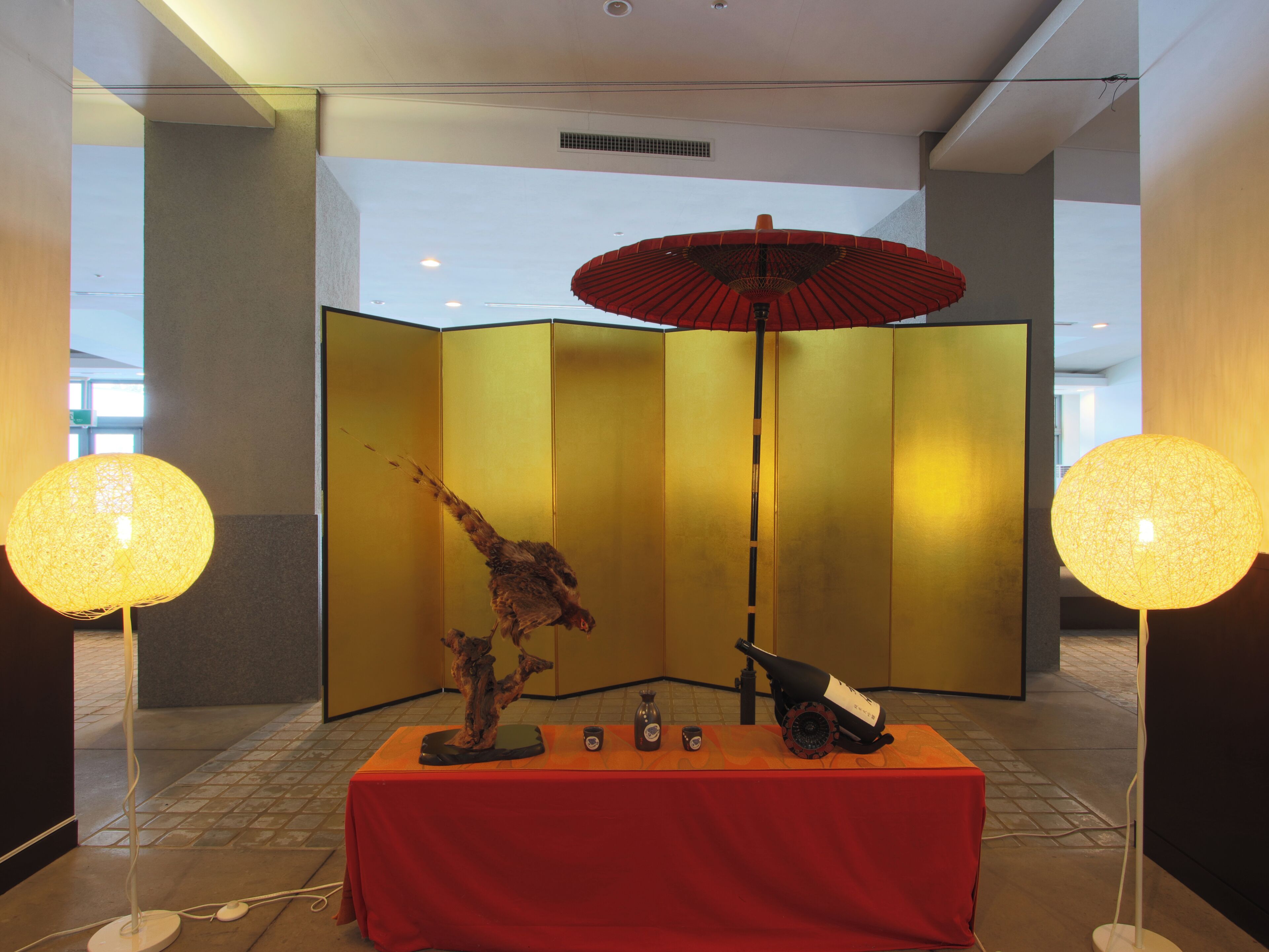 A room with a red table, a decorative tree, a bottle, and a red umbrella.