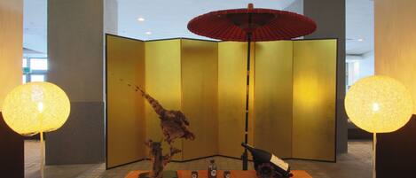 A room with a red table, a decorative tree, a bottle, and a red umbrella.