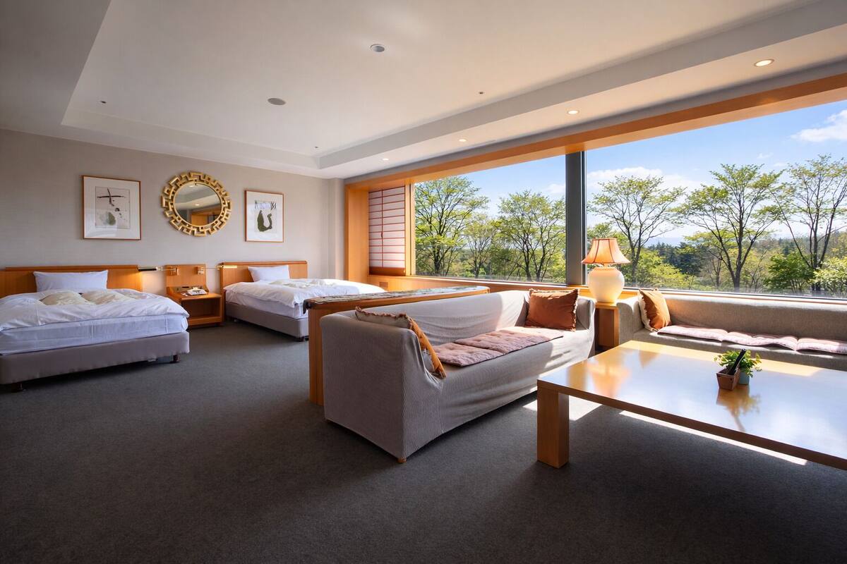 Une chambre d’hôtel avec deux lits, un canapé, une table et une grande fenêtre donnant sur la forêt.