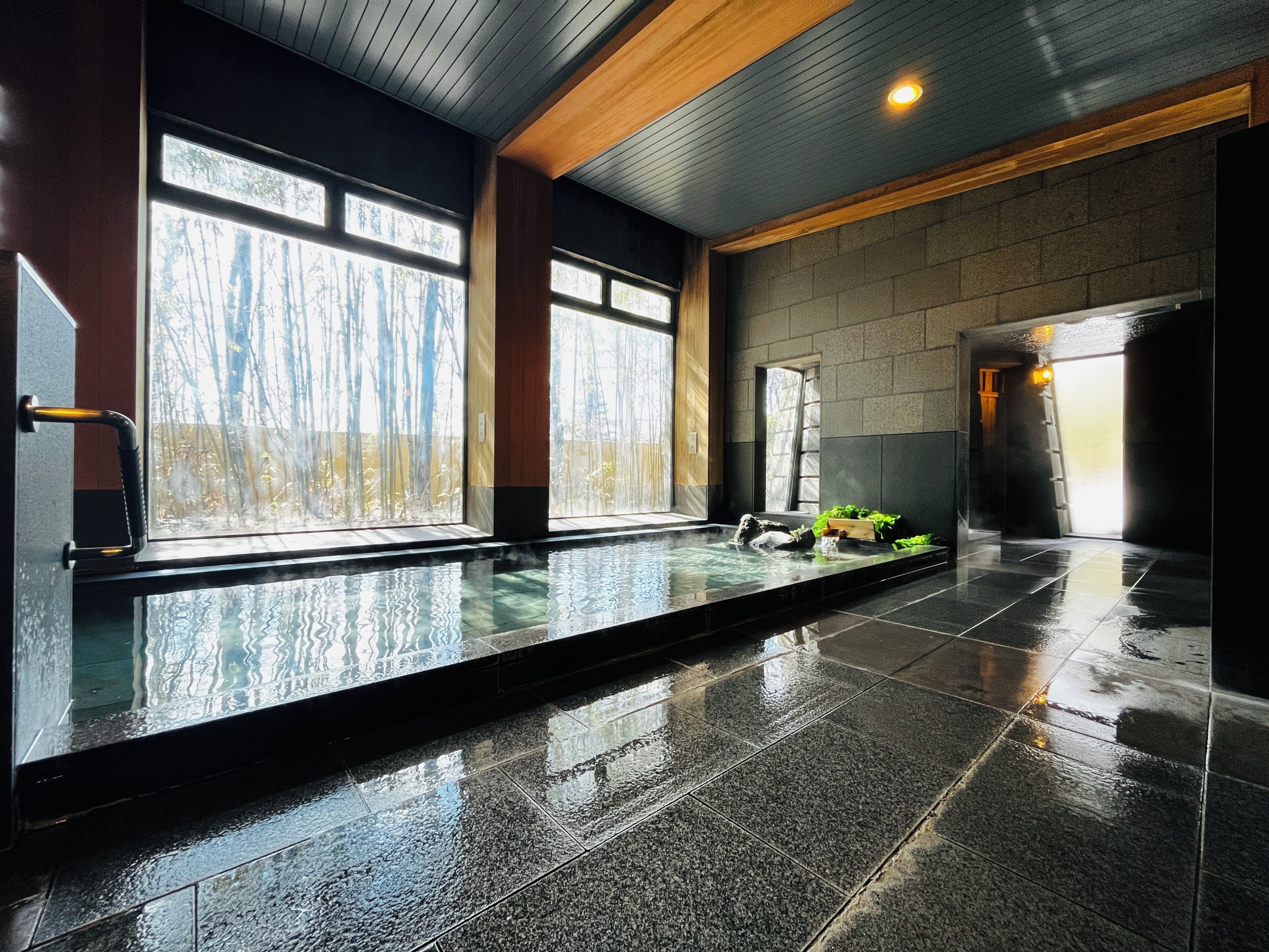 Piscina interior moderna com paredes de vidro transparente, piso revestido e teto de madeira.
