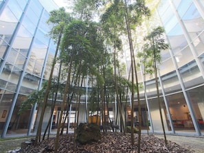 A modern building with a glass facade, a central courtyard with tall bamboo trees, and a rock feature. - Daitofuji resorthotel (Oyama)
