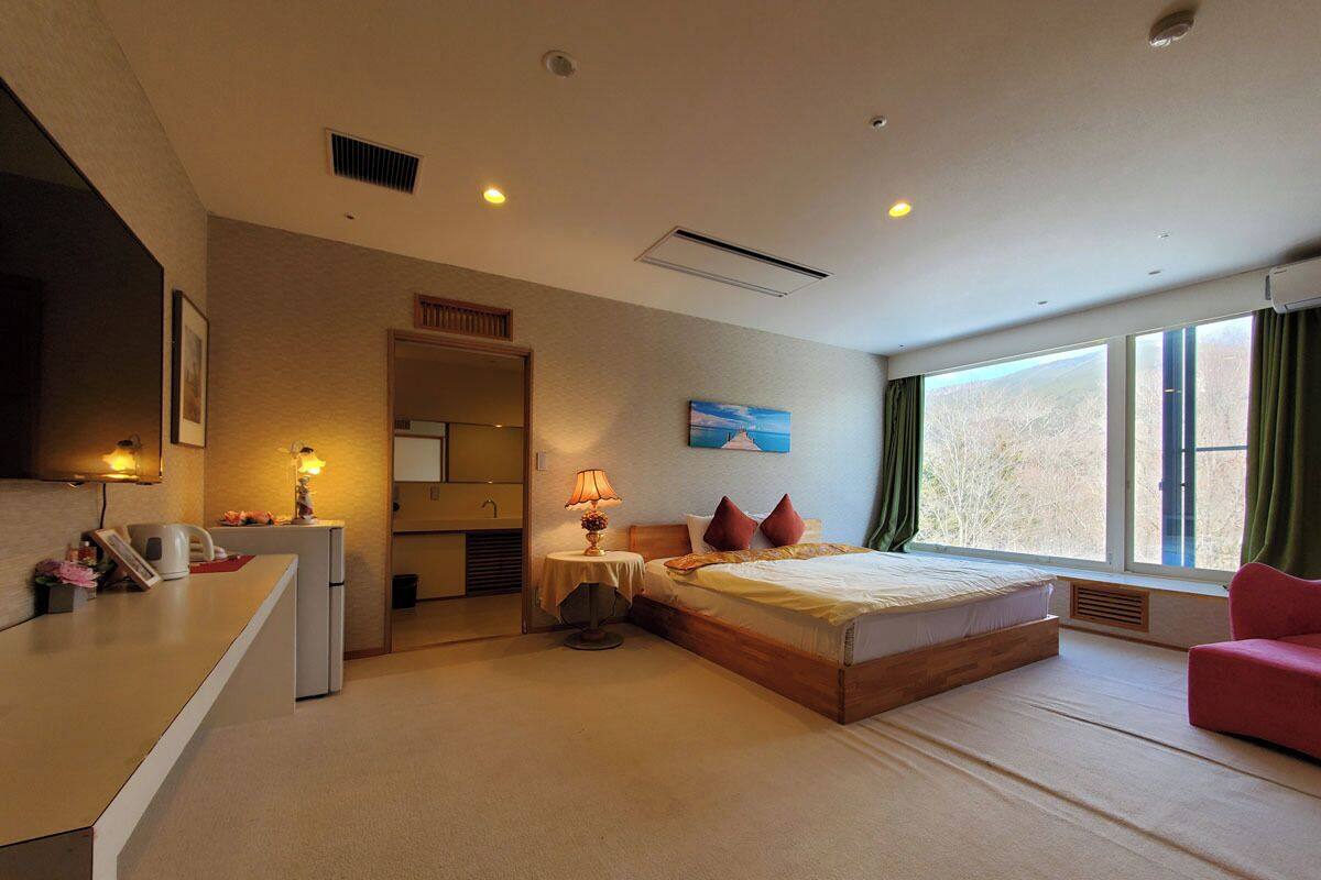 Une chambre d’hôtel avec un lit, un bureau, une chaise, une fenêtre avec des rideaux et un tableau au mur.