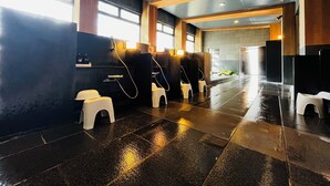 Eine öffentliche Toilette mit Einzelkabinen, einem Händetrockner und einem gefliesten Boden.