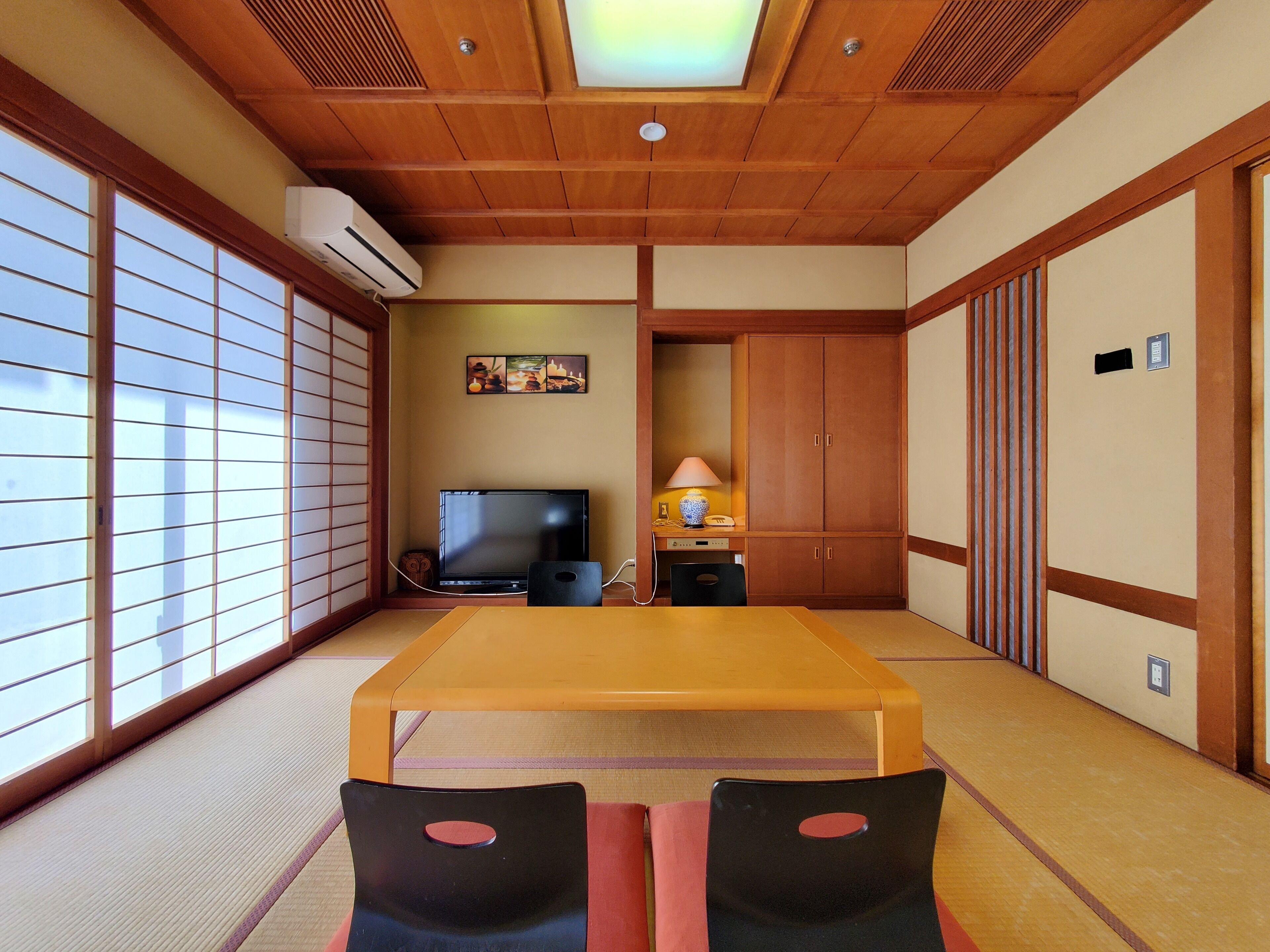 Una habitación japonesa tradicional con suelo de tatami, televisor, escritorio y puertas correderas.