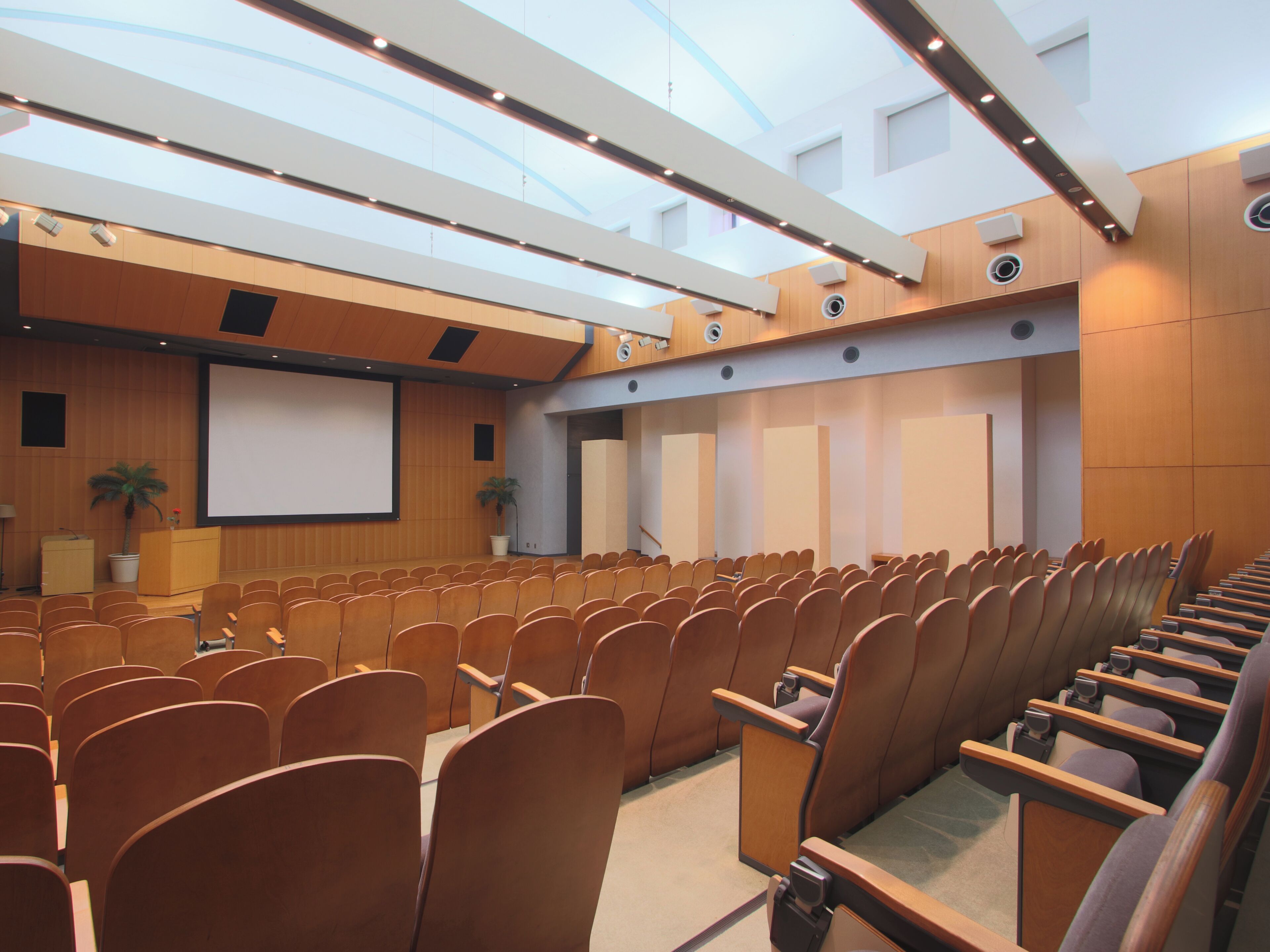 Een congreszaal met rijen stoelen, een spreekgestoelte en een groot scherm.