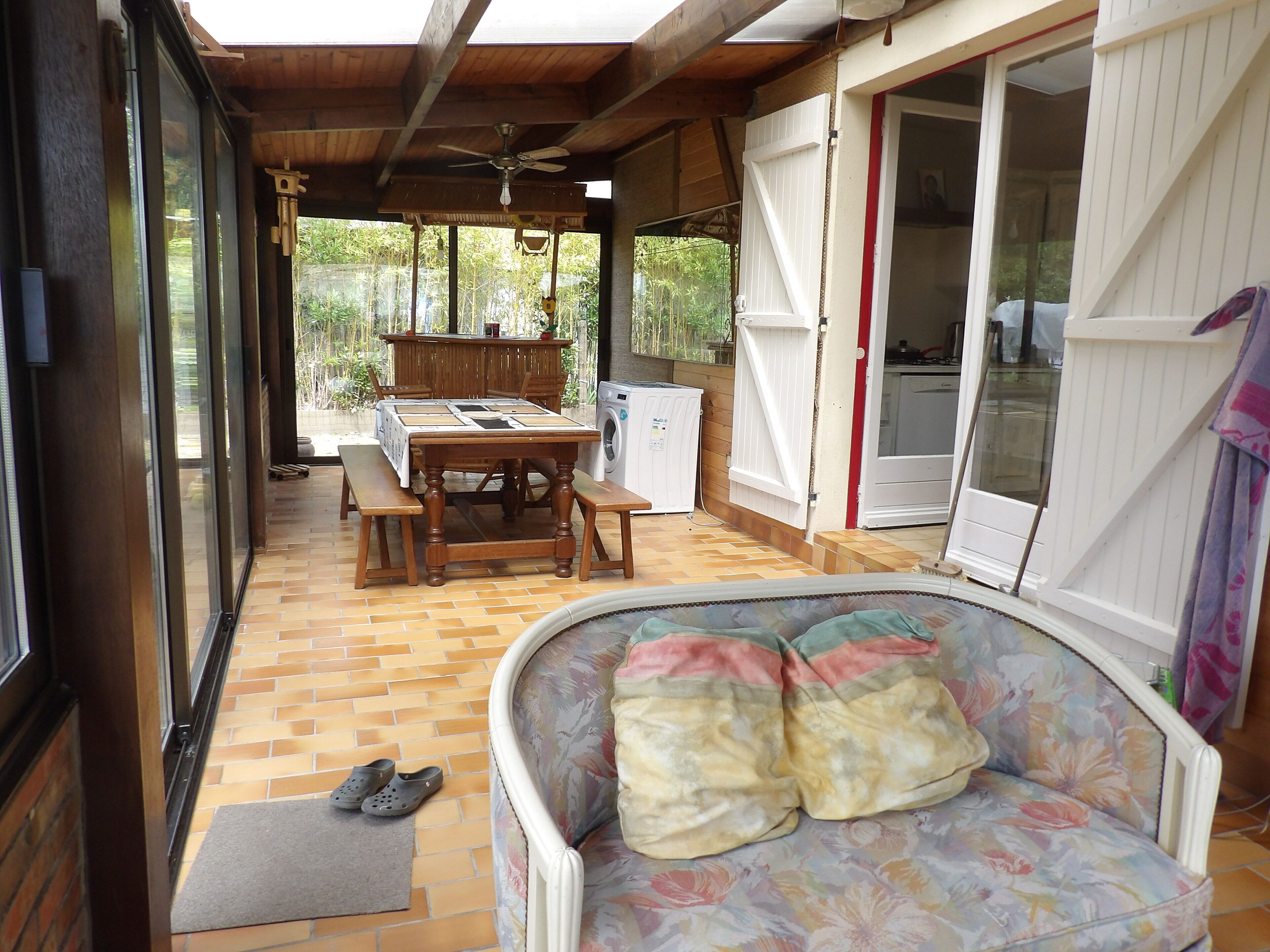 Eine überdachte Terrasse mit Holztisch, Stühlen, einer Couch und einer Waschmaschine.