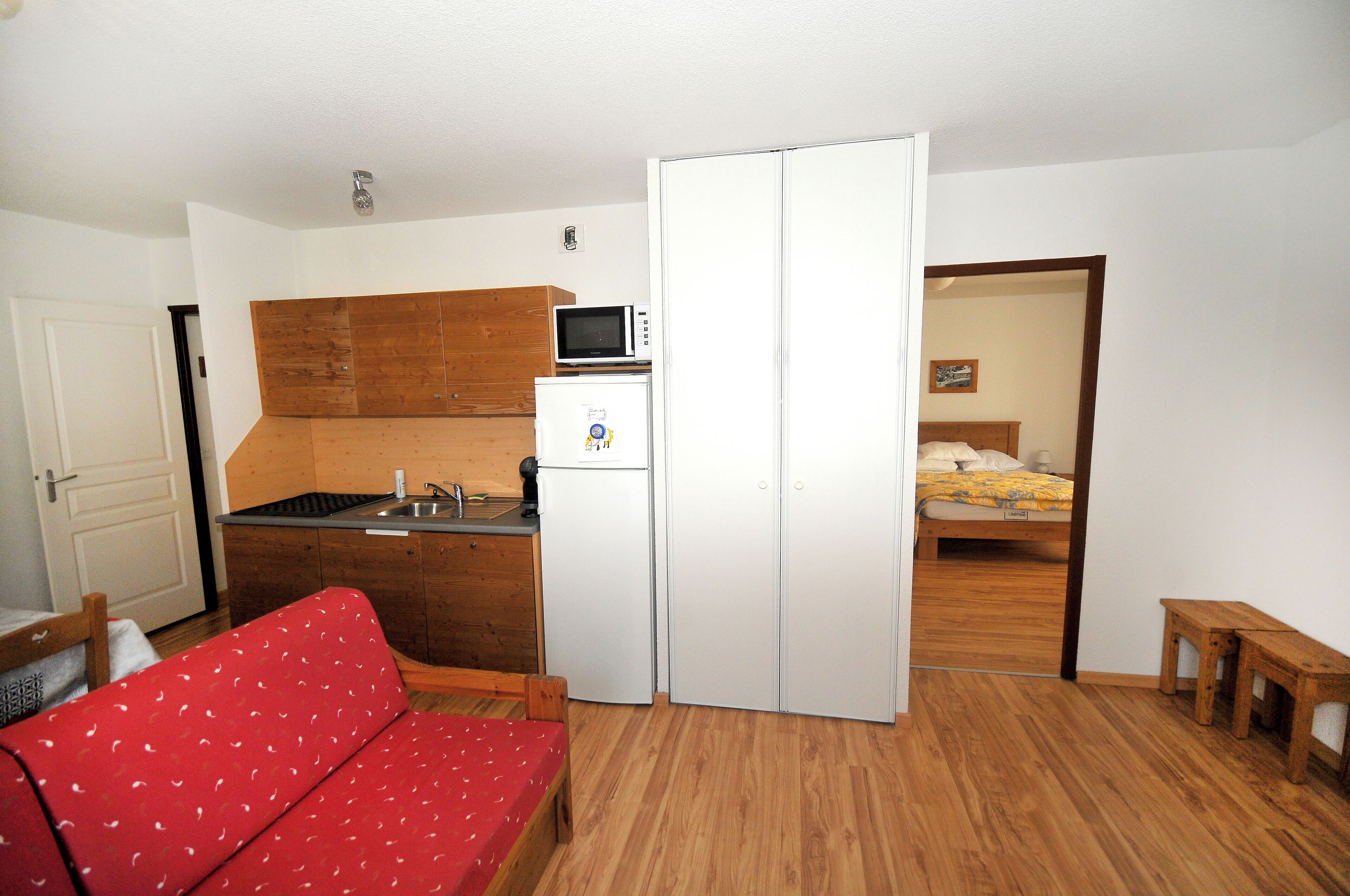 Een kleine kamer met een kitchenette, een bed en een rode slaapbank.