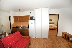A compact room with a kitchenette, a bed, and a red sofa. - Mountain apartment at the start of cross-country skiing and hiking trails (Villar-d'Arêne)